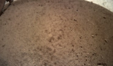 InSight flipped open the lens cover on its Instrument Context Camera (ICC) on November 30, 2018, and captured this view of Mars. Located below the deck of the InSight lander, the ICC has a fisheye view, creating a curved horizon. Some clumps of dust are still visible on the camera’s lens. One of the spacecraft’s footpads can be seen in the lower right corner. The seismometer’s tether box is in the upper left corner. Image credit: NASA / JPL-Caltech.