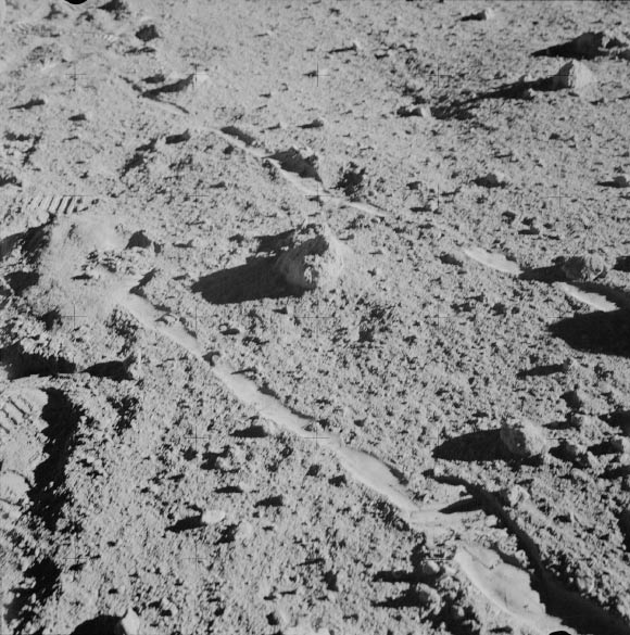 The two Moon-exploring crew men of the Apollo 14 lunar landing mission photographed and collected the large rock pictured just above the exact center of this picture. The rock, casting a shadow off to the left, is the lunar breccia 14321. It lies between the wheel tracks made by the modular equipment transporter (MET) or rickshaw-type portable workbench. A few prints of the lunar overshoes of the crew members are at the left. This photo was made near the boulder field near the rim of Cone Crater. Image credit: NASA.