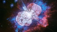 Astronomers have monitored the Eta Carinae binary system for more than two decades. It has been prone to violent outbursts, including an episode in the 1840s during which ejected material formed the bipolar bubbles seen here. Now, using Hubble’s Wide Field Camera 3 (WFC3) instrument to probe the nebula in ultraviolet light, they have uncovered the glow of magnesium embedded in warm gas (shown in blue) in places they had not seen it before. The luminous magnesium resides in the space between the dusty bipolar bubbles and the outer shock-heated nitrogen-rich filaments (shown in red). The streaks visible in the blue region outside the lower-left lobe are a striking feature of the image. These streaks are created when the star’s light rays poke through the dust clumps scattered along the bubble’s surface. Wherever the ultraviolet light strikes the dense dust, it leaves a long, thin shadow that extends beyond the lobe into the surrounding gas. Image credit: NASA / ESA / Hubble / N. Smith, University of Arizona / J. Morse, BoldlyGo Institute.