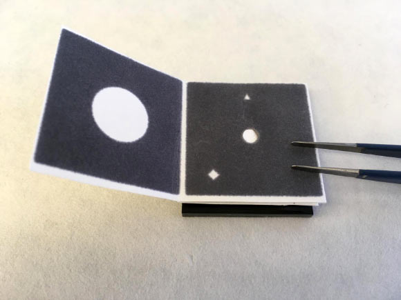 The paper device is folded and unfolded in steps to filter the nucleic acids of pathogens from wastewater samples, then a biochemical reaction with preloaded reagents detects whether the nucleic acid of SARS-CoV-2 infection is present; the results are visible to the naked eye: a green circle indicating positive and a blue circle negative. Image credit: Cranfield University.