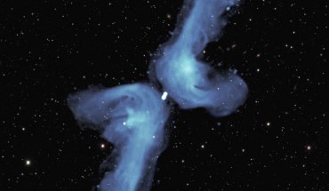 PKS 2014-55 is classified as ‘X-shaped’ because of its appearance in previous relatively blurry images. The detail provided in this radio image obtained with the MeerKAT telescope indicates that its shape is best described as a double boomerang. Two powerful jets of radio waves, indicated in blue color, each extend 2.5 million light-years into space. Eventually, they are ‘turned back’ by the pressure of tenuous intergalactic gas. As they flow back towards the central galaxy, they are deflected by its relatively high gas pressure into the shorter, horizontal, arms of the boomerang. The background image shows visible light from myriad galaxies in the distant Universe. Image credit: NRAO / AUI / NSF / SARAO / DES.
