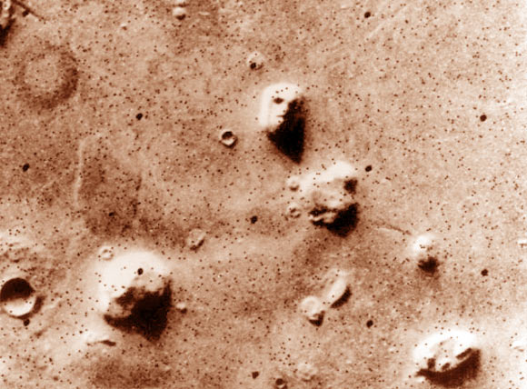 NASA’s Viking 1 orbiter photographed the Cydonia region in the northern latitudes of Mars on July 25, 1976 while searching for a landing site for the Viking 2 lander. The speckled appearance of the image is due to missing data, called bit errors, caused by problems in transmission of the photographic data from Mars to Earth. Bit errors comprise part of one of the ‘eyes’ and ‘nostrils’ on the eroded rock that resembles a human face near the center of the image. Shadows in the rock formation give the illusion of a nose and mouth. Planetary geologists attribute the origin of the formation to purely natural processes. The feature is 1.5 km across, with the Sun angle at approximately 20 degrees. The picture was taken from a range of 1,873 km. Image credit: NASA / JPL.