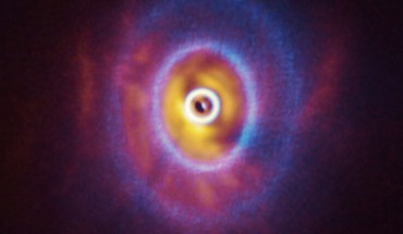 This composite image shows both ALMA and SPHERE/VLT observations of the disk around GW Orionis. The ALMA image (blue) shows the disk’s ringed structure, with the innermost ring (part of which is visible as an oblong dot at the very center of the image) separated from the rest of the disk. The SPHERE observations (orange-red) allowed the astronomers to see for the first time the shadow of this innermost ring on the rest of the disk, which made it possible for them to reconstruct its warped shape. Image credit: ALMA / ESO / NAOJ / NRAO / ESO / University of Exeter / Kraus et al.