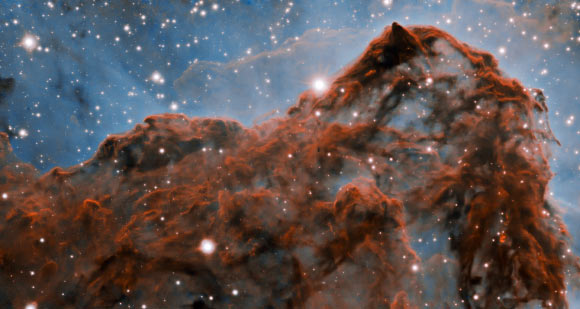 A 5-light-year-long section of the western wall in the Carina Nebula, as observed with adaptive optics on the Gemini South telescope. This mountainous section of the nebula reveals a number of unusual structures including a long series of parallel ridges that could be produced by a magnetic field, a remarkable almost perfectly smooth wave, and fragments that appear to be in the process of being sheared off the cloud by a strong wind. There is also evidence for a jet of material ejected from a newly-formed star. The exquisite detail seen in the image is in part due to a technology known as adaptive optics, which resulted in a ten-fold improvement in the resolution of the research team’s observations. Image credit: International Gemini Observatory / NOIRLab / NSF / AURA / Patrick Hartigan, Rice University / Travis Rector, University of Alaska Anchorage / Mahdi Zamani / Davide de Martin.