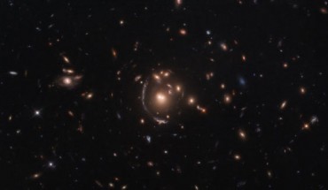 This Hubble image shows the strong-lensing galaxy cluster SDSS J0901+1814. The lensed star-forming galaxy LRG-3-817 is seen as a long arc to the left of the cluster’s central galaxy. The color image was made from separate exposures taken in the visible and infrared regions of the spectrum with Hubble’s Wide Field Camera 3 (WFC3). Five filters were used to sample various wavelengths. The color results from assigning different hues to each monochromatic image associated with an individual filter. Image credit: Hubble / ESA / NASA / S. Allam et al.