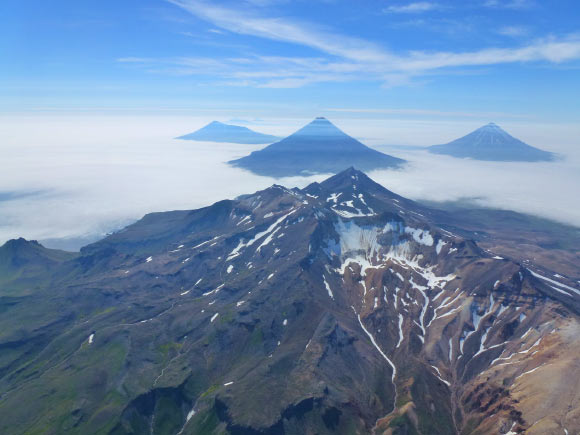 An aerial oblique photo of the volcanoes in the Islands of Four Mountains, Alaska, taken in July 2014. In the center is the summit of Mount Tana. Behind Tana are (left to right) Herbert, Cleveland, and Carlisle volcanoes. Image credit: John Lyons / USGS.