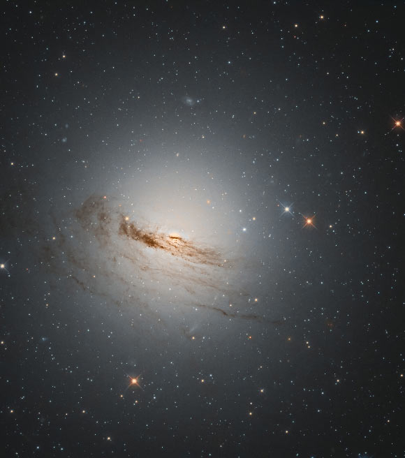 This Hubble image shows NGC 1947, a lenticular galaxy located some 40 million light-years away in the constellation Dorado. The color image of NGC 1947 was made from separate exposures taken in the visible and infrared regions of the spectrum with Hubble’s Wide Field Camera 3 (WFC3). Two filters were used to sample various wavelengths. The color results from assigning different hues to each monochromatic image associated with an individual filter. Image credit: NASA / ESA / Hubble / D. Rosario / L. Shatz.