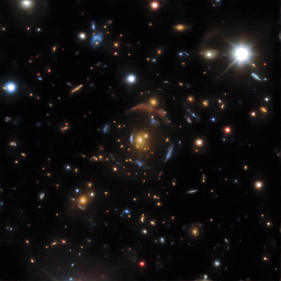 An example of a gravitational lens found in the DESI Legacy Surveys data. There are four sets of lensed images in DESI-090.9854-35.9683, corresponding to four distinct background galaxies -- from the outermost giant red arc to the innermost bright blue arc, arranged in four concentric circles. All of them are gravitationally lensed by the orange galaxy at the very center. Image credit: NOIRLab.