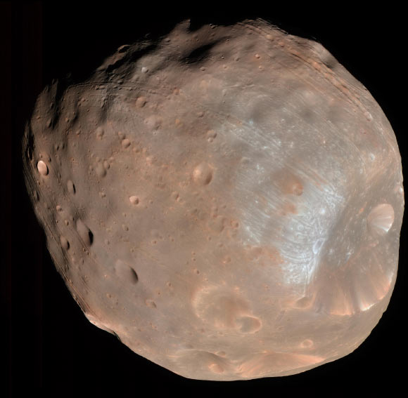 The High Resolution Imaging Science Experiment (HiRISE) camera on NASA’s Mars Reconnaissance Orbiter captured this image of the larger of Mars’ two moons, Phobos, on March 23, 2008. The image was taken from a distance of about 6,800 km (about 4,200 miles). It is presented in color by combining data from the camera’s blue-green, red, and near-infrared channels. The illuminated part of Phobos seen in the image is about 21 km (13 miles) across. The most prominent feature is the large crater Stickney in the lower right. With a diameter of 9 km (5.6 miles), it is the largest feature on Phobos. Image credit: NASA / JPL-Caltech / University of Arizona.