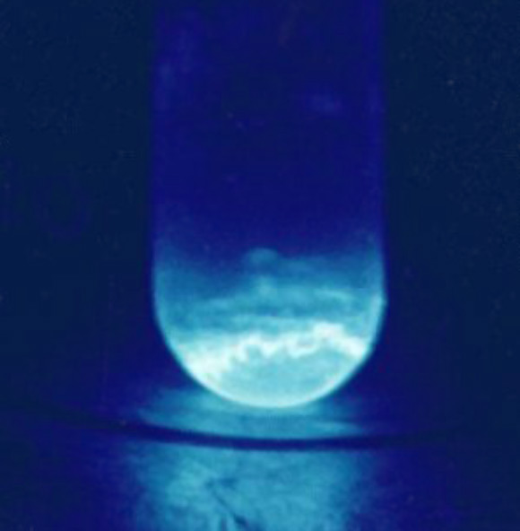 Quartz vial containing 300 micrograms of einsteinium-253. The illumination produced is a result of the intense radiation from einsteinium-253, which alpha decays with a half-life of 20.5 days. Image credit: R.G. Haire, U.S. Department of Energy.
