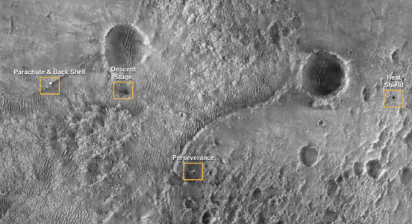 This first image of NASA’s Perseverance Rover on the surface of Mars from the High Resolution Imaging Experiment (HiRISE) camera aboard NASA’s Mars Reconnaissance Orbiter shows the many parts of the Mars 2020 mission landing system that got the rover safely on the ground. The image was taken on February 19, 2021. The image points out the locations of the parachute and back shell, the descent stage, the Perseverance rover, and the heat shield. Each inset shows an area about 200 m (650 feet) across. The rover itself sits at the center of a blast pattern created by the hovering descent stage that lowered it there using the sky crane maneuver. The descent stage flew off to crash at a safe distance, creating a V-shaped debris pattern that points back toward the rover. Earlier in the landing sequence, Perseverance jettisoned its heat shield and parachute, which can be seen on the surface in the separate locations illustrated. These objects are highly visible on the surface of Mars now but will become dustier with time and slowly fade into the background over years. HiRISE will continue to image the Perseverance landing site to track the progress of the rover and changes with the other pieces of hardware that accompanied it. Image credit: NASA / JPL-Caltech / University of Arizona.