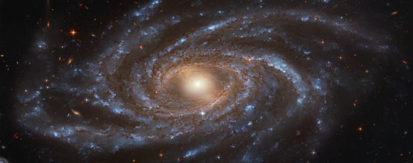 This Hubble image shows NGC 2336, a barred spiral galaxy located 109 million light-years away in the constellation of Camelopardalis. The color image was made from separate exposures taken in the visible and near-infrared regions of the spectrum with Hubble’s Advanced Camera for Surveys (ACS). Three filters were used to sample various wavelengths. The color results from assigning different hues to each monochromatic image associated with an individual filter. Image credit: NASA / ESA / Hubble / V. Antoniou / Judy Schmidt.