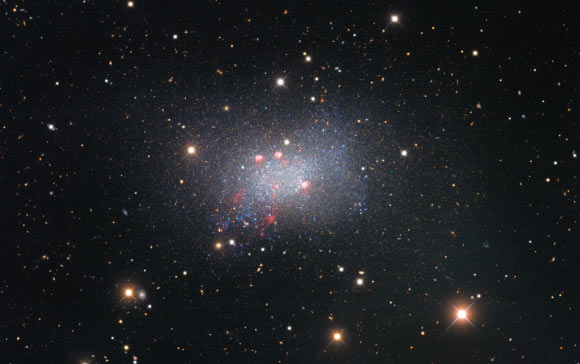 This image of the irregular dwarf galaxy Sextans B, taken by the Nicholas U. Mayall 4-m Telescope, features red-colored star-forming regions near the galaxy’s center; surrounding the galaxy are several bright stars that are located much closer to us in our Milky Way Galaxy, identified by the crisscross patterns created by light interacting with the structure of the telescope, as well as numerous fuzzy-looking background galaxies that appear small because they are much farther away than Sextans B. Image credit: KPNO / NOIRLab / NSF / AURA / P. Massey, Lowell Observatory / G. Jacoby / K. Olsen / C. Smith, AURA & NSF / T.A. Rector, University of Alaska Anchorage & NSF’s NOIRLab / M. Zamani, NSF’s NOIRLab / D. de Martin, NSF’s NOIRLab.