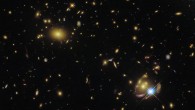 This Hubble image shows a massive galaxy cluster (bottom left corner) and three images of the gravitationally lensed galaxy SGAS 0033+02. The color image was made from separate exposures taken in the visible and infrared regions of the spectrum with Hubble’s Wide Field Camera 3 (WFC3). Five filters were used to sample various wavelengths. The color results from assigning different hues to each monochromatic image associated with an individual filter. Image credit: NASA / ESA / Hubble / E. Wuyts.