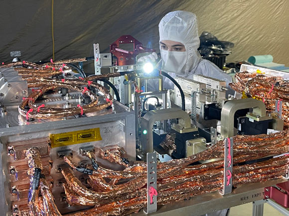 An engineer inspects the radio frequency (RF) panel of NASA’s Europa Clipper in a cleanroom at the Johns Hopkins Applied Physics Laboratory. The RF panel hosts all the RF subsystem electronics and an intricate routing network of switches, filters, and waveguides, which carry the RF signal to and from eight antennas distributed around the spacecraft. Image credit: Credits: Johns Hopkins Applied Physics Laboratory.