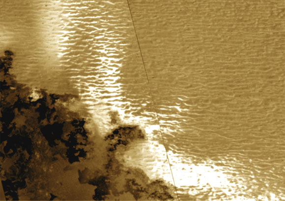 Potential dunes on Jupiter’s moon Io: the dark material (lower left) is recently emplaced lava flows, while the repeated, line-like features dominating the image are potential dunes; the bright, white areas may be newly emplaced grains as the lava flows vaporize adjacent frost. Image credit: NASA / JPL-Caltech / Rutgers University.