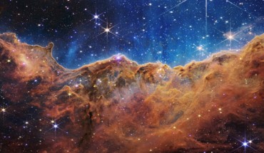 This landscape of ‘mountains’ and ‘valleys’ speckled with glittering stars is actually the edge of the Carina Nebula, a huge star-forming region some 7,500 light-years away in the constellation of Carina. Captured in infrared light by Webb, this image reveals for the first time previously invisible areas of star birth. Called the Cosmic Cliffs, Webb’s seemingly 3D picture looks like craggy mountains on a moonlit evening. In reality, it is the edge of the giant, gaseous cavity within the Carina Nebula, and the tallest ‘peaks’ in this image are about 7 light-years high. The cavernous area has been carved from the nebula by the intense ultraviolet radiation and stellar winds from extremely massive, hot, young stars located in the center of the bubble, above the area shown in this image. Image credit: NASA / ESA / CSA / STScI.