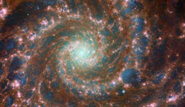 Messier 74, a grand design spiral galaxy located 32 million light-years away in the constellation of Pisces, shines at its brightest in this combined optical/mid-infrared image, featuring Webb and Hubble data. The red colors mark dust threaded through the arms of the galaxy, lighter oranges being areas of hotter dust. The young stars throughout the arms and the nuclear core are picked out in blue. Heavier, older stars towards the galaxy’s center are shown in cyan and green, projecting a spooky glow from the core of Messier 74. Bubbles of star formation are also visible in pink across the arms. Image credit: NASA / ESA / CSA / Webb / Hubble / J. Lee / PHANGS-JWST Team / R. Chandar / J. Schmidt.