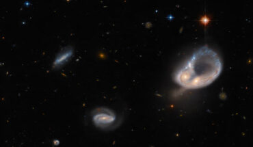 Two galaxies in the Arp-Madore 417-391 system (right) form a ring shape, which is narrow and blue, and the cores of the two galaxies form a bulge on the ring’s side. Two smaller spiral galaxies appear left of center as well as a few stars. Image credit: NASA / ESA / Hubble / Dark Energy Survey / DOE / FNAL / DECam / CTIO / NOIRLab / NSF / AURA / J. Dalcanton.
