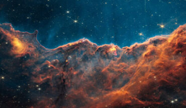 This Webb image shows the Cosmic Cliffs, a region at the edge of a gigantic, gaseous cavity within the stellar nursery NGC 3324. The image is divided horizontally by an undulating line between a orange-burgundy cloudscape forming a nebula along the bottom portion and a comparatively blue upper portion. Image credit: NASA / ESA / CSA / STScI / J. DePasquale, STScI.