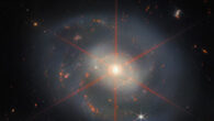 This Webb image shows NGC 7469, a barred spiral galaxy some 206 million light-years away in the constellation of Pegasus. The galaxy has blue-purple hues with orange-red regions filled with stars. NGC 7469’s companion galaxy, IC 5283, is partly visible in the lower left portion of this image. Also visible is large diffraction spike, which appears as a star pattern over the central region of the galaxy. Lots of stars and galaxies fill the background scene. Image credit: NASA / ESA / CSA / Webb / L. Armus / A.S. Evans.