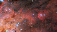 This new Hubble image shows part of the Tarantula Nebula, which is located about 163,000 light-years away in the southern constellation of Dorado: wispy, nebulous clouds extend from the lower-left of the image; at the top and right the dark background of space can be seen through the sparse nebula; along the left and in the corner are many layers of brightly-colored gas and dark, obscuring dust; a cluster of small, bright blue stars in the same corner expands out across the image. Image credit: NASA / ESA / Hubble / C. Murray / E. Sabbi / Y.-H. Chu.