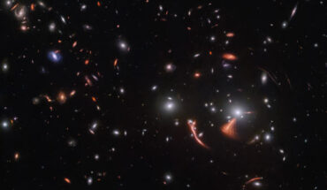 To the lower right of this Webb image is the lensing cluster SDSS J1226+2149 with a very large and bright elliptical galaxy at its center; thin, reddish, stretched-out arcs surround it; one arc is thick and much brighter; another red galaxy is large and warped, just next to the cluster core. Image credit: NASA / ESA / CSA / Webb / J. Rigby.