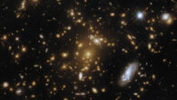 This Hubble image shows eMACS J1823.1+7822, a massive cluster of galaxies some 9 billion light-years away in the constellation of Draco. The central cluster is mostly made of bright elliptical galaxies that are surrounded by a warm glow. Close to the cluster core is the stretched, distorted arc of a galaxy, gravitationally lensed by the cluster. Image credit: NASA / ESA / Hubble / H. Ebeling.
