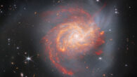 This Webb image shows NGC 3256, a spiral galaxy located 131 million light-years away in the constellation of Vela. The galaxy’s core is radiating very brightly. Streaks of dust glow intensely red, in the center and across most of the galaxy. This gas is surrounded by a dark gray halo made of the galaxy’s stars. The halo stretches out into a tidal tail at the upper-left, and another at the bottom. Image credit: NASA / ESA / CSA / Webb / L. Armus / A. Evans.