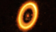 This ALMA image shows the young planetary system PDS 70. The system features a star at its center, around which the planet PDS 70b (highlighted with a solid yellow circle) is orbiting. On the same orbit as PDS 70b, indicated by a solid yellow ellipse, Balsalobre-Ruza et al. detected a cloud of debris (circled by a yellow dotted line) that could be the building blocks of a new planet or the remnants of one already formed. The ring-like structure that dominates the image is a circumstellar disk of material, out of which planets are forming. There is in fact another planet in this system: PDS 70c, seen at 3 o’clock right next to the inner rim of the disk. Image credit: ALMA / ESO / NAOJ / NRAO / Balsalobre-Ruza et al.