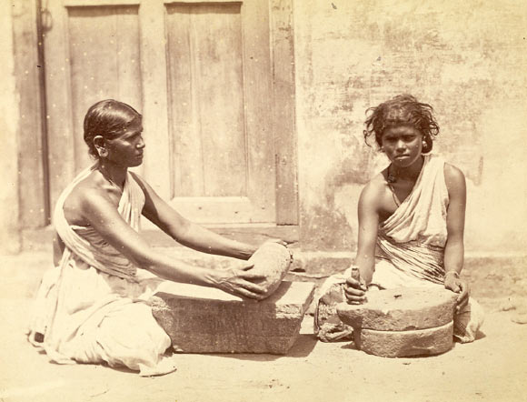 This photograph, shown at the Vienna Universal Exhibition of 1873, shows at left a woman crushing spices with a stone roller on a grinding slab similar to those from Oc Eo (but without separately carved feet). The woman at right is grinding ragi (finger millet of Late Harappan African origin), a grain cultivated as a food staple in Southern India, between two round millstones. Photo taken at Madras (Chennai) in Tamil Nadu by Nicholas and Curths in c. 1870, from the Archaeological Survey of India. Image credit: British Library Board.