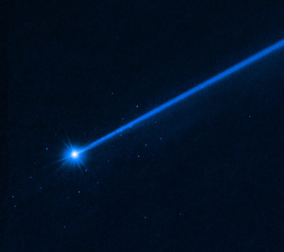 This Hubble image of Dimorphos was taken on December 19, 2022, nearly four months after the asteroid was impacted by NASA’s DART mission. Dimorphos has a blue dust tail extending diagonally to the upper right. A cluster of blue dots surrounds the asteroid. These are boulders that were knocked off the asteroid. Image credit: NASA / ESA / D. Jewitt, UCLA.