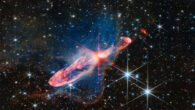 This Webb image shows a pair of actively forming stars, known as Herbig-Haro 46/47, in high-resolution near-infrared light. To find them, trace the bright pink and red diffraction spikes until you hit the center. The stars are within the orange-white splotch. They are buried deeply in a disk of gas and dust that feeds their growth as they continue to gain mass. The disk is not visible, but its shadow can be seen in the two dark, conical regions surrounding the central stars. Image credit: NASA / ESA / CSA / Joseph DePasquale, STScI.