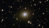 This Hubble image shows various distant galaxies in the constellation of Cetus: most of the galaxies are very small, but there are a few larger galaxies and some stars where detail can be made out; in the center there is an elliptical galaxy with a brightly glowing core and a broad disk; a reddish, warped ring of light, thicker at one side, surrounds its core; a small galaxy intersects the ring as a bright dot. Image credit: NASA / ESA / Hubble / H. Nayyeri / L. Marchetti / J. Lowenthal.