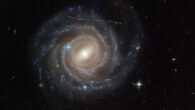 This Hubble image of the barred spiral galaxy UGC 12158 looks like someone took a white marking pen to it. In reality it is a combination of time exposures of a foreground asteroid moving through Hubble’s field-of-view, photobombing the observation of the galaxy. Several exposures of the galaxy were taken, what is evidence in the dashed pattern. The asteroid appears as a curved trail due to parallax: because Hubble is not stationary, but orbiting Earth, and this gives the illusion that the faint asteroid is swimming along a curved trajectory. The uncharted asteroid is in inside the asteroid belt in our Solar System, and hence is 10 trillion times closer to Hubble than the background galaxy. Image credit: NASA / ESA / Hubble / Pablo García Martín, UAM / Joseph DePasquale, STScI / Alex Filippenko, UC Berkeley.