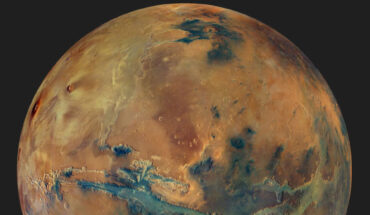 This image from Mars Express’ High Resolution Stereo Camera shows the globe of Mars set against a dark background. The disk of the planet features yellow, orange, blue and green patches, all with an overall muted grey hue, representing the varying composition of the surface. Image credit: ESA / DLR / FU Berlin / G. Michael / CC BY-SA 3.0 IGO.