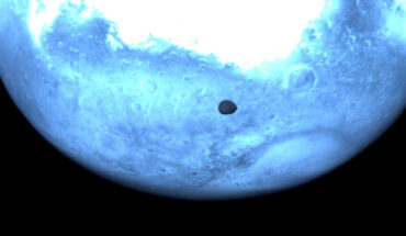 Mars appears light blue in this near-infrared image from Hera’s Hyperscout H hyperspectral imager, acquired during the mission’s March 12 gravity-assist flyby of Mars, with Deimos seen ahead of it. The spacecraft was approximately 1,000 km from the 12.4-km-diameter Deimos when this image was acquired. In the background a variety of Martian features can be observed. At the top of the image is the bright Terra Sabaea region, close to the Martian equator, outlined by darker regions about it, with the 450 km-diameter Huygen crater to the bottom right of Terra Sabaea and the 460-km-diameter Schiaparelli crater to its left. To the bottom right of the Martian disk is Hellas Basin, among the largest known impact craters in the Solar System with a diameter of 2,300 km and a depth of more than 7 km. Image credit: ESA.