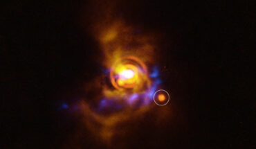 This image shows a possible substellar companion orbiting the young star V960 Mon. The candidate object was found with ESO’s Very Large Telescope (VLT), using its new Enhanced Resolution Imager and Spectrograph (ERIS). The new ERIS data are shown here in orange, overlaid on older images of the dusty disk as seen with the VLT’s SPHERE instrument (yellow) and ALMA (blue). Image credit: ESO / A. Dasgupta / ALMA / ESO / NAOJ / NRAO / Weber et al.