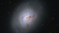 This Hubble image reveals the lenticular galaxy NGC 1266; reddish-brown clumps and filaments of dust partially obscure the galaxy’s full face, while red, blue, and orange light from distant galaxies shines through its diffuse outer regions and dots the inky-black background. Image credit: NASA / ESA / K. Alatalo, STScI / G. Kober, NASA & Catholic University of America.
